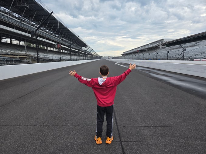 A middle school-aged student wearing a red jacket, black pants, and orange shoes stands facing away…