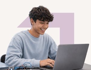 A male student wearing a blue long-sleeved sweater is smiling and looking at the screen of a laptop. The background features a purple arrow pointing to the top right.